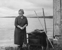 Kvinne står ved en vedovn ved oppdemt innsjø