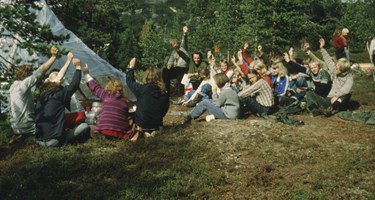 Personer sitter ved campingplass og tar håndsopprekning