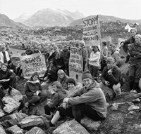 En gruppe sittende unge menn og kvinner i turklær med demonstrasjonsplakater. I bakgrunnen fjellandskap.  