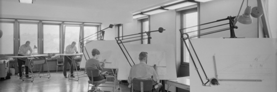 Tegnesal, med to personer i bakgrunnen som tegner på vertikale bord, og to personer som tegner på de to bakerste av tre horisontale bord med montert arm med vinkel/linjal